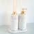 Kit Lavabo Santorini com dois dispensadores decorativos em tons de branco e dourado, um com difusor e outro com bomba de sabonete.
