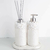 Kit lavabo Santorini com dois recipientes brancos decorados com pedras brancas e suporte, um com difusor e outro com bomba para sabonete.