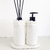 Kit Lavabo Santorini com dois recipientes brancos decorados com pedras brancas, um com bomba e outro com varetas aromáticas.