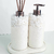 Conjunto de produtos de lavabo com dois dispensers, um para sabonete líquido e outro para difusor de aromas, decorados com pedras brancas e base em formato oval.