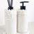 Kit lavabo Santorini com frascos brancos e tampa preta, decorados com pedras brancas na parte superior.