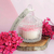 Aurora Candle in a decorative glass holder surrounded by pink flowers.