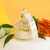 Vela Aurora de Mel e Limão em um recipiente de vidro decorativo, com etiqueta visível e flores ao fundo.