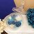 Vela aromática decorativa com flores em tons de azul e branco, em um recipiente de vidro.