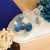 Vela aromática Vela Aurora - Cedro Real em recipiente de vidro com flores em tons de azul e branco.