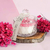 Vela aromática Lumière com fragrância de flor de cerejeira, decorada com flores rosa e apresentada em um recipiente de vidro sobre uma base de madeira.