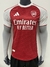 camisa modelo jogador do arsenal i temporada 25/26 nas cores vermelha com as mangas brancas e as tradicionais 3 listras da adidas em vermelho nos ombros