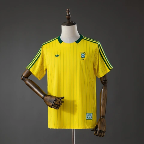 Esta é a camisa retrô amarela da seleção brasileira da coleção Terrace Icons da Adidas Originals, que se destaca pelas finas listras verticais em tom escuro e pelo clássico logo Trefoil verde no peito
