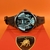SmartWatch JS50 Pro Max exibindo sua tela com informações de bateria e clima, sobre uma caixa vermelha com um logotipo de touro.