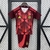 Kit infantil Alemanha II 2025 vermelho com camisa e short pendurados em cabide contra fundo de grade metálica