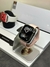 smartwatch applewatch serie 10 na cor rosa num suporte metálico e de fundo uma caixa branca e um outro applewatch na cor branco
