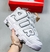 Tênis Nike Air More Uptempo na cor branca, com detalhes em preto, segurado por uma mão, em frente a uma caixa da Nike.