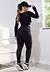 Modelo de costas vestindo um conjunto de calça legging e cropped preto com detalhes em tela, em ambiente moderno.