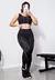 Modelo usando um conjunto fitness preto com detalhes em branco, composto por cropped e calça legging, em ambiente de academia.