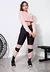 Modelo usando um conjunto fitness composto por calça legging preta com detalhes em rosê e um cropped rosê, posando em ambiente de academia.
