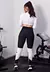 Modelo usando um conjunto fitness composto por calça legging preta e cropped branco, em um ambiente de academia.