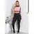 Mulher usando um conjunto fitness com calça legging preta e blusa cropped rosa com detalhes pretos, em um ambiente iluminado.