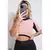 Mulher segurando um celular, vestindo um conjunto fitness com cropped rosa e calça legging preta.