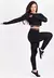 Modelo usando conjunto fitness preto composto por calça legging, cropped e top de telinha, em pose ativa.