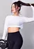 Modelo usando um cropped branco de manga longa em tecido dry fit, segurando um peso, com cabelo preso em um coque.
