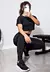 Modelo vestindo um conjunto fitness preto com cropped e calça legging, posando em uma academia.