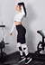 Modelo usando um conjunto fitness de calça legging preta e cropped branco em um ambiente de academia.