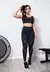 Modelo usando o conjunto Suiça Fitness, composto por cropped preto e calça legging preta com detalhes em branco.