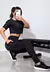 Modelo vestindo conjunto fitness cropped preto com calça legging com bolso tela, posando em um ambiente de treino.
