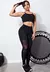 Modelo vestindo um conjunto fitness feminino preto com legging e top de transparência, posando em um ambiente de treino.