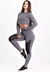 Modelo vestindo um conjunto fitness cinza com calça legging de tela DryFit e cropped de manga longa, posando em ambiente claro.