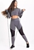 Mulher usando um conjunto fitness composto por calça legging com tela e cropped de manga longa na cor cinza aço, segurando faixas de resistência.
