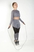 Modelo usando calça legging com tela e cropped de manga longa em cinza aço, pulando corda.