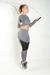Modelo usando um conjunto fitness cinza com calça legging e cropped, pulando corda.
