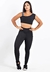 Mulher usando um conjunto de calça legging preta e cropped, com detalhes em branco, em fundo branco.
