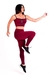 Modelo vestindo conjunto fitness marsala com cropped e calça legging de cintura alta, realizando movimento de exercício.