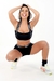 Modelo usando conjunto fitness preto com cropped e short, fazendo pose divertida.
