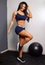 Conjunto fitness marinho com cropped e short, modelo em pose sorridente em ambiente de academia.