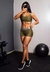 Modelo usando um conjunto fitness verde militar, composto por cropped e short, em um ambiente de academia.
