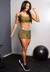 Modelo usando um conjunto fitness verde militar, composto por cropped e short, em ambiente de academia.