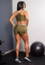 Modelo usando conjunto fitness verde militar com cropped e short, de costas, em ambiente de academia.