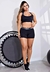 Modelo vestindo um conjunto fitness preto, composto por cropped e short, ao lado de um trampolim.