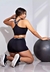 Modelo usando conjunto fitness preto com cropped e short, posando ao lado de uma bola de exercícios.
