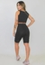 Modelo usando um conjunto fitness preto, composto por cropped e bermuda, com detalhes de tatuagens visíveis.