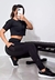 Modelo usando calça legging fitness preta com bolso em tela, posando com a mão na cintura.
