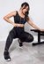 Calça legging fitness preta com detalhe lateral em branco, usada por uma mulher em pose de exercício em ambiente de academia.