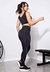 Mulher usando calça legging fitness preta com detalhe lateral em branco, em um ambiente de academia.