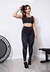 Mulher usando calça legging fitness preta com detalhe lateral em vivo branco e top cropped, em ambiente de academia.