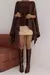 Mulher usando blusa estilo boho marrom com detalhes de textura, combinada com saia curta bege e botas de cano alto em couro.