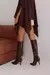 Mulher usando blusa estilo boho marrom com detalhes de textura, combinada com saia curta bege e botas de cano alto em couro.