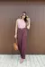 Modelo usando uma blusa rosa e calça de cintura alta, alfaiataria com detalhe na frente na cor vinho.